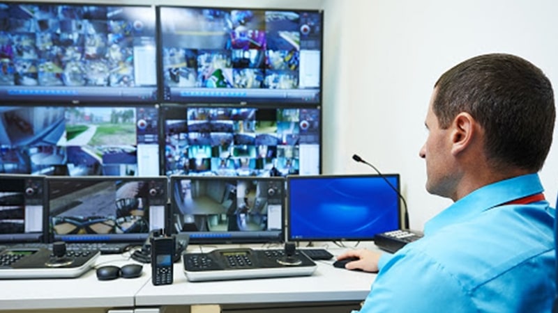 Un hombre en el centro de control de seguridad del campus supervisando el campus a través de un videowall que muestra las imágenes de las cámaras en directo