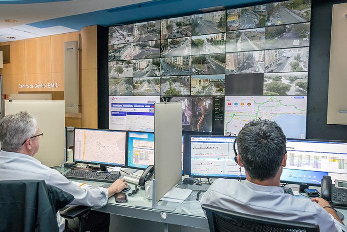 Sala de control de la EMT de Madrid con dos trabajadores supervisando las carreteras y los datos mostrados en un videowall
