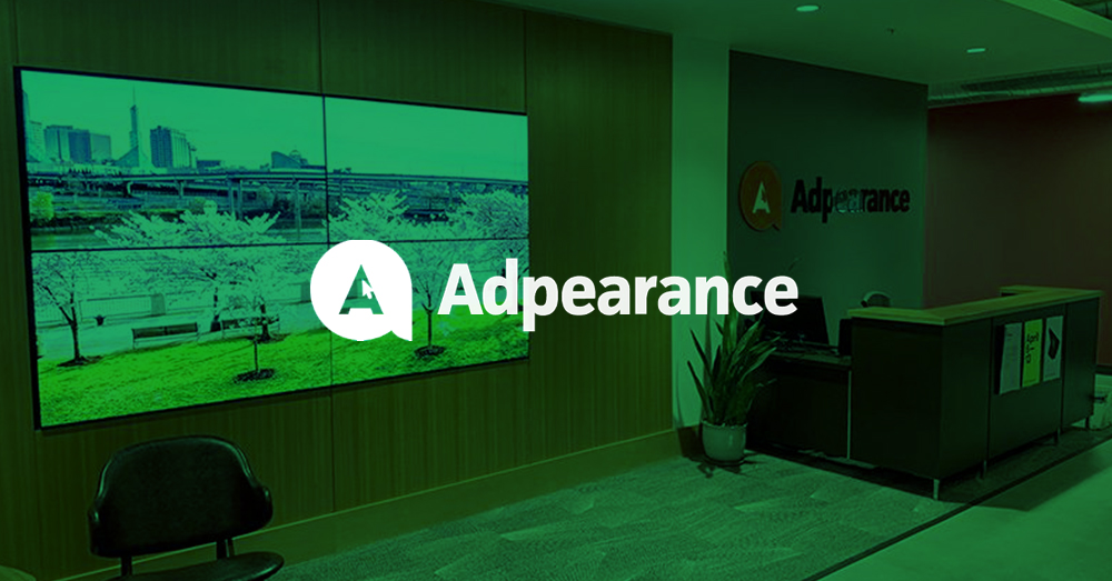 Vestíbulo vacío de Adpearance, con una pared de vídeo alimentada por Userful que muestra fotografías detrás de una zona de estar, y un mostrador de recepción con el logotipo de Adpearance en la pared de detrás con una superposición verde y el logotipo
