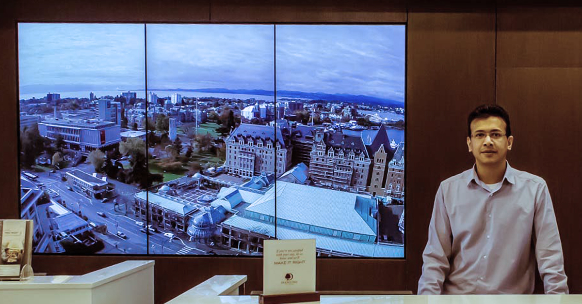 Recepcionista de DoubleTree by Hilton y pared de vídeo de 3 paneles detrás de él mostrando lugares emblemáticos de Victoria, Canadá