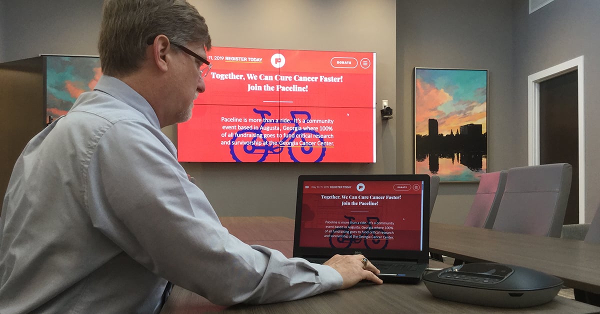 Sala de reuniones del Medical College of Georgia, con un hombre utilizando su portátil y el Userful para mostrar una página web en un videowall detrás de él