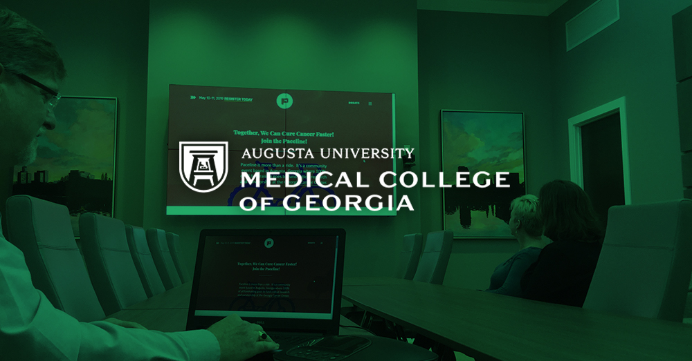 Sala de reuniones del Medical College of Georgia, con un hombre que utiliza su ordenador portátil y el Userful para mostrar una página web en una pared de vídeo detrás de él con una superposición verde y el logotipo