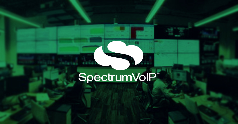 Centro de operaciones de red SpectrumVoIP vacío con muchas estaciones de trabajo y una pared de vídeo más grande que muestra paneles de datos con superposición verde y logotipo