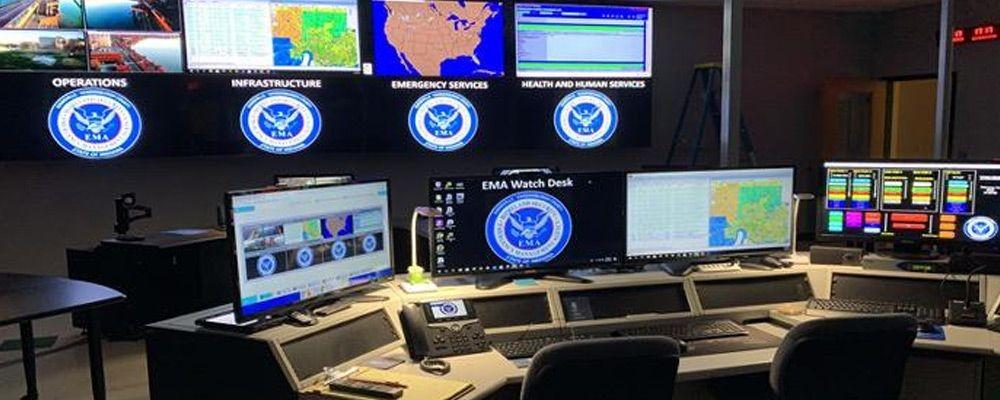 Centro de control vacío de la EMA con puestos de trabajo y videowall que muestra fotos, datos y mapas