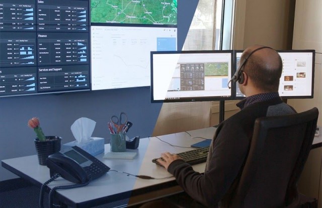 Empleado en la sala de control en su mesa de trabajo tecleando, mirando un videowall que muestra paneles de datos y mapas