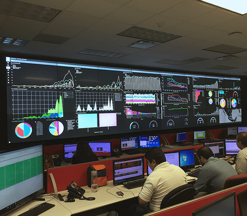 Empleados trabajando en una sala de control en puestos de trabajo con videowalls que muestran paneles de datos