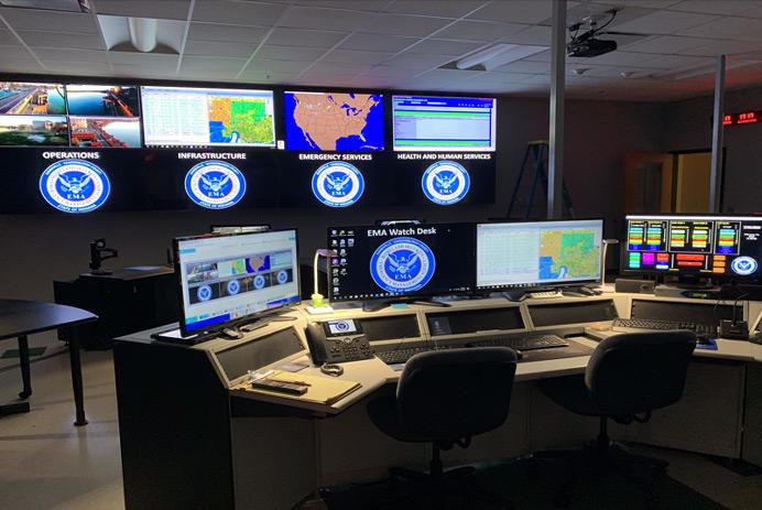 Sala de control de la EMA vacía, con estación de trabajo y un videowall que muestra fotografías, datos y mapas