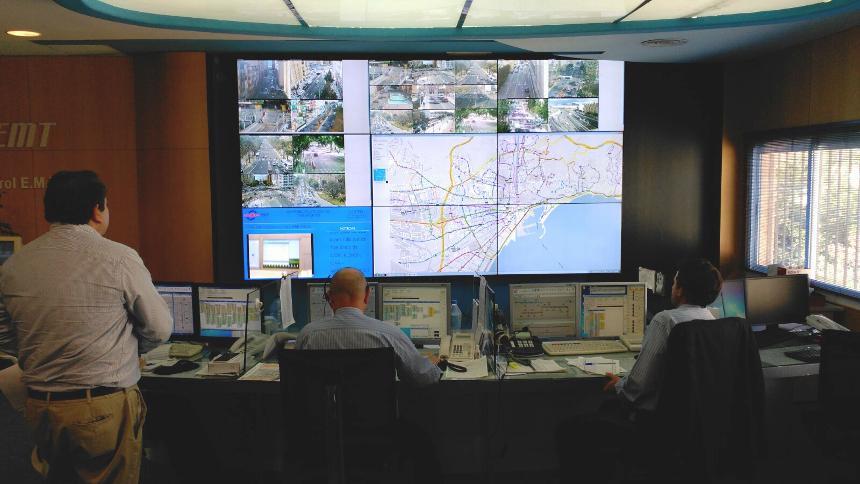 Centro de control de la EMT con trabajadores que supervisan las condiciones de tránsito a través de sus puestos de trabajo y un videowall que muestra las rutas de tránsito, imágenes en directo y datos