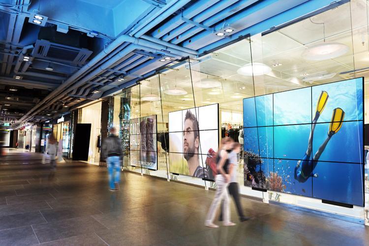 Múltiples paredes de vídeo de gran tamaño en el pasillo de un centro comercial, que muestran anuncios y arte