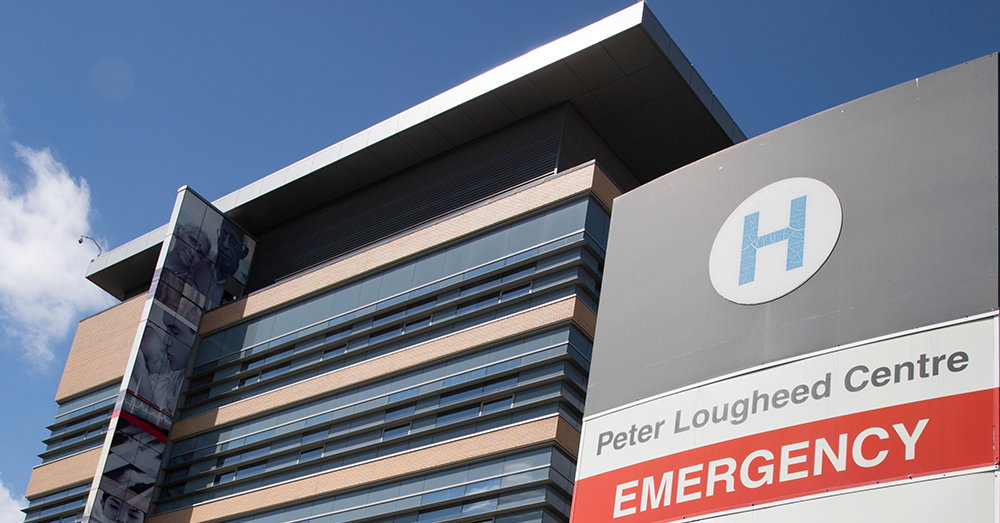 Una foto de la señal de emergencia del Peter Lougheed Center Hospital, y del edificio del hospital contra un cielo azul
