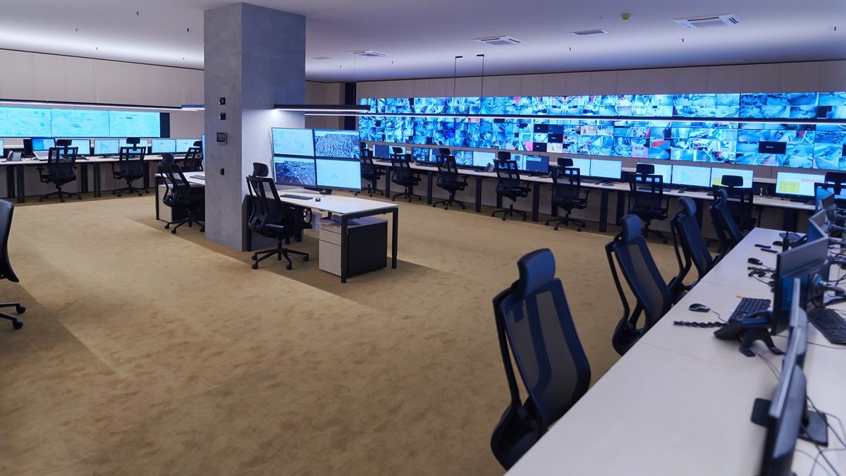 Empty office space with multiple workstations and video wall monitors displaying security camera feeds and area surveillance.