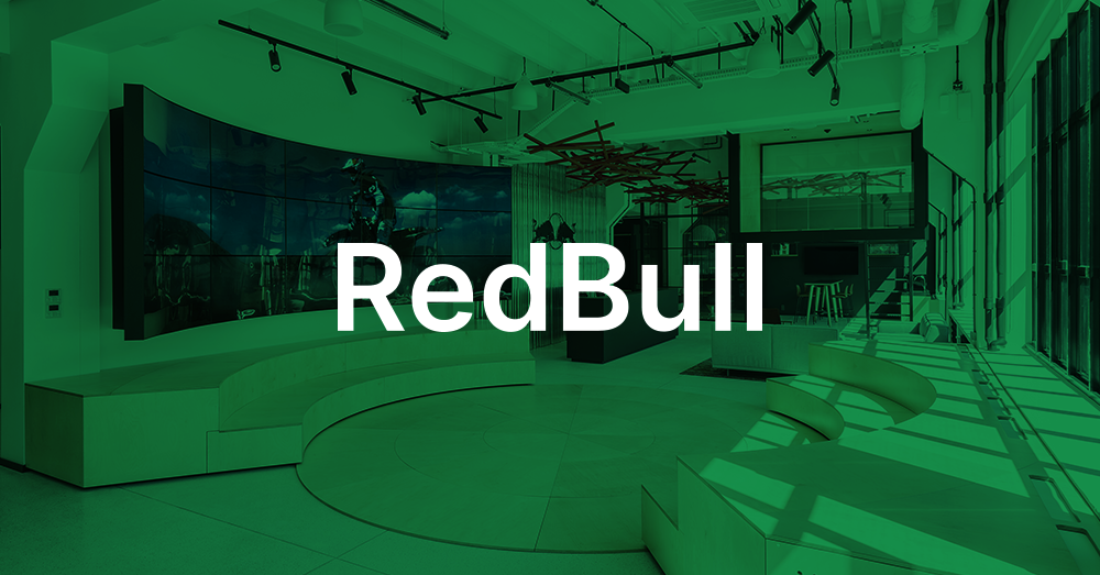 Vestíbulo de la sede central de Redbull Polonia, con zona de estar en forma de escalera, mostrador de recepción y una pared de vídeo curvada que muestra un anuncio de Red Bull con sobreimpresión verde y el logotipo