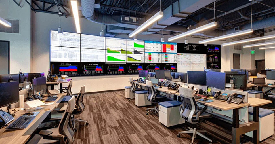 Centro de operaciones de red SpectrumVoIP vacío con muchas estaciones de trabajo y un muro de vídeo más grande que muestra paneles de datos